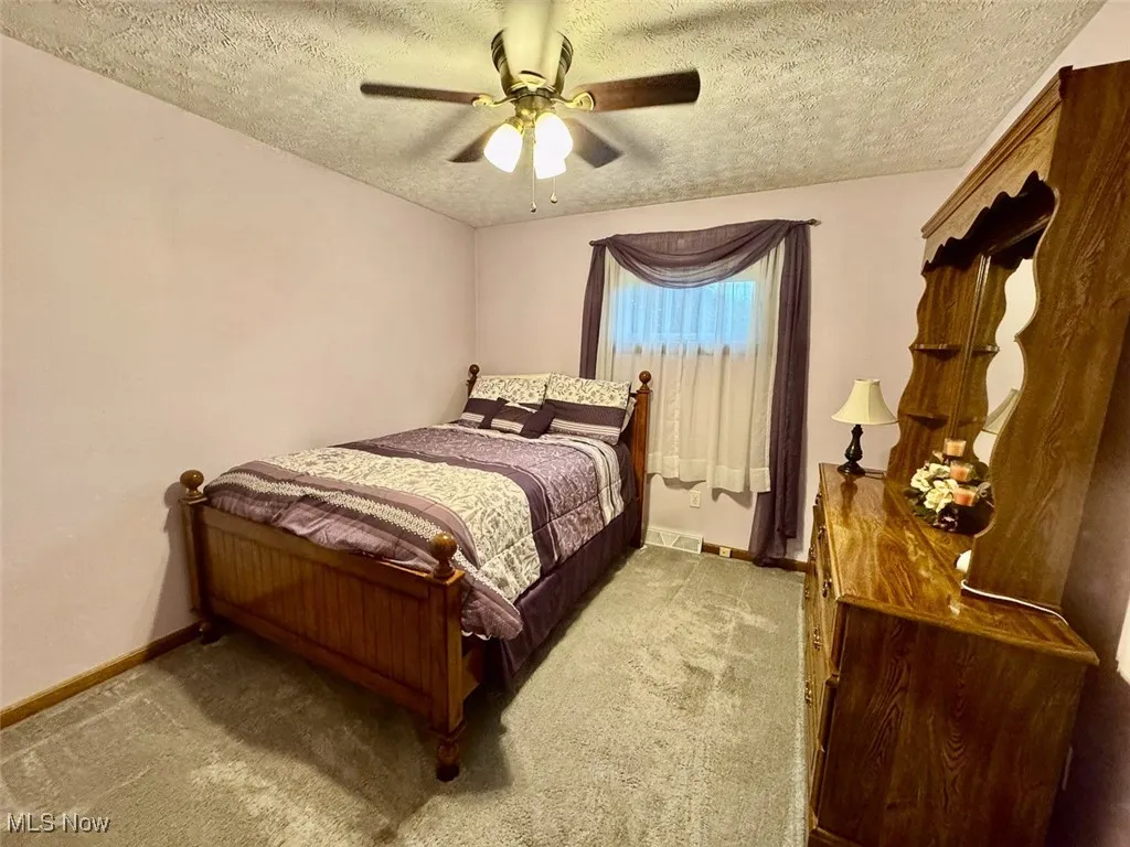Bedroom with a textured ceiling, carpet flooring, and a ceiling fan