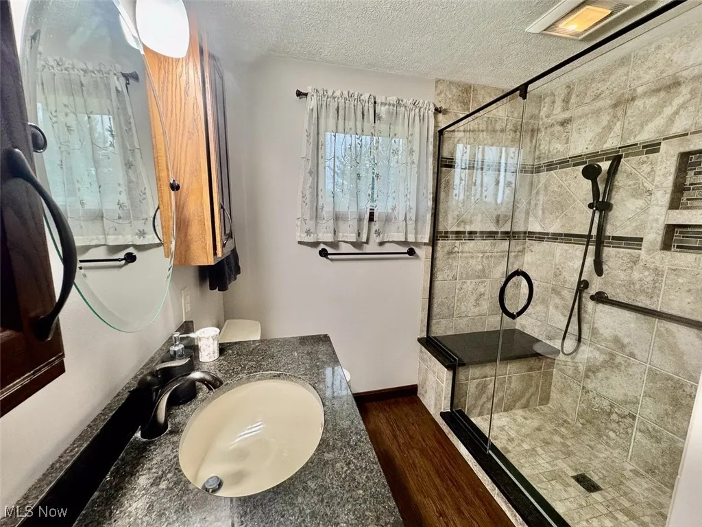 Full bath featuring a textured ceiling, a shower stall, wood finished floors, and vanity