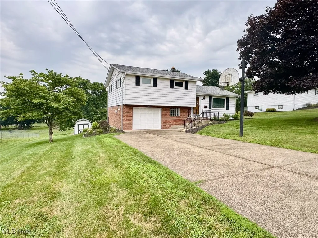 Split level home with brick siding, an attached garage, a shed, a front lawn, and concrete driveway