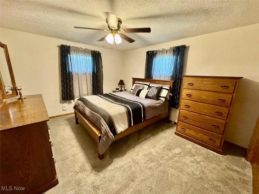 Bedroom featuring a textured ceiling, light colored carpet, and a ceiling fan