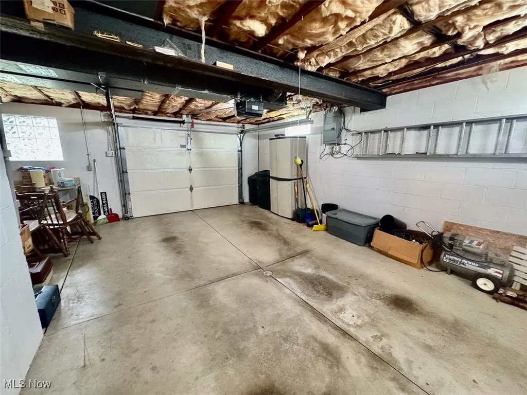 Garage featuring concrete block wall, electric panel, and a garage door opener