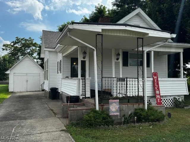 Bungalow-style home featuring a porch, driveway, a detached garage, an outbuilding, and a shingled roof