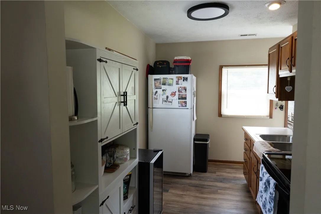 Kitchen with freestanding refrigerator, electric range, dark wood-style floors, light countertops, and a textured ceiling