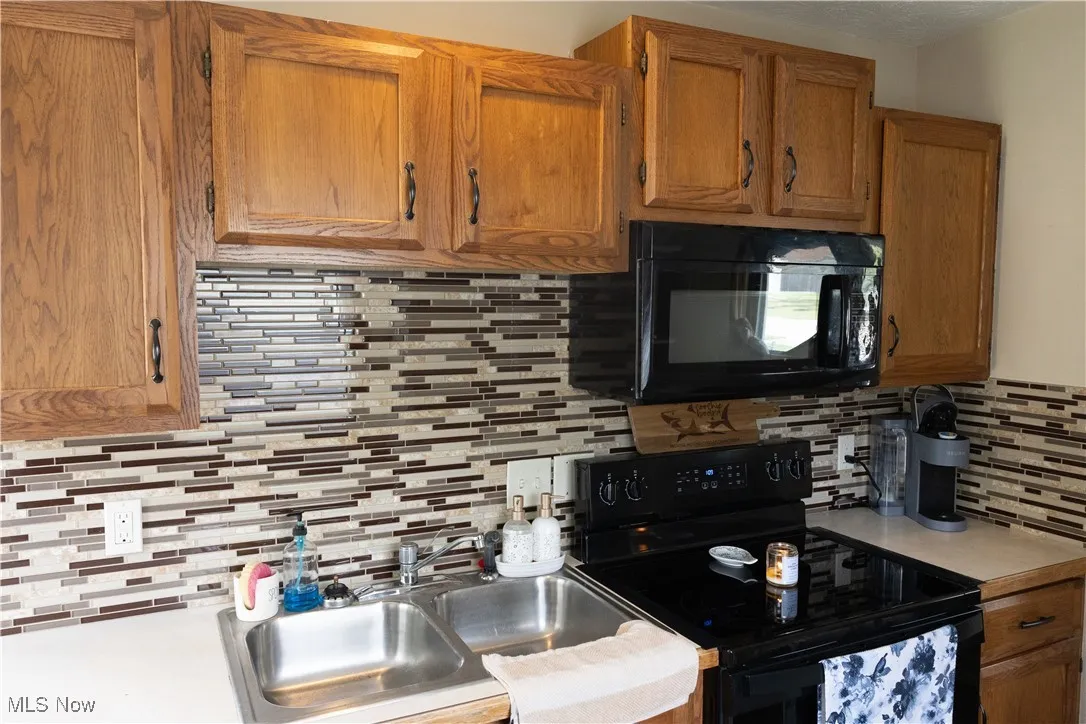 Kitchen with black appliances, tasteful backsplash, light countertops, and brown cabinets