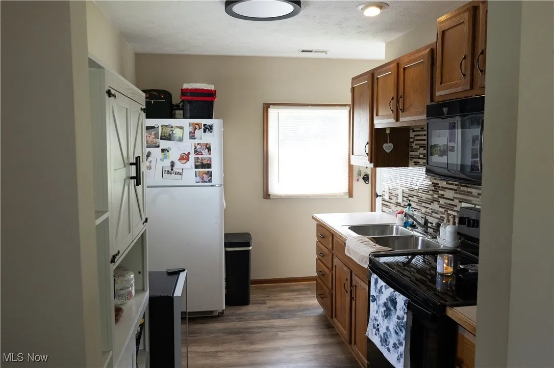 Kitchen with black appliances, decorative backsplash, dark wood-type flooring, brown cabinetry, and a textured ceiling
