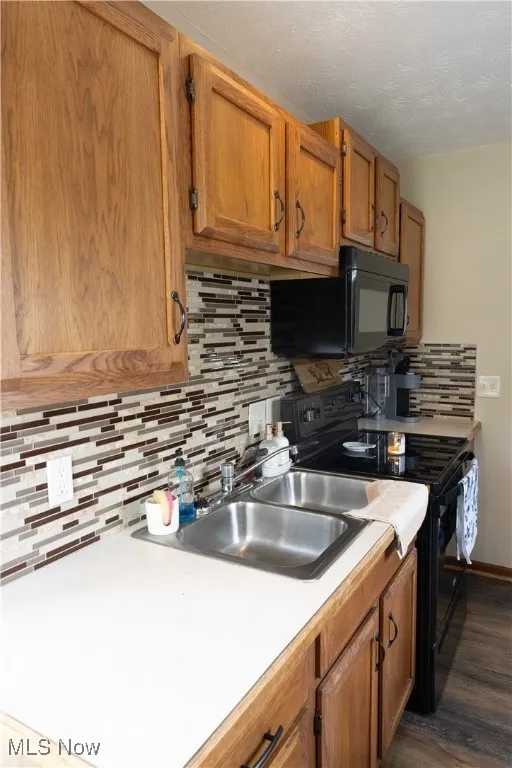 Kitchen featuring black appliances, tasteful backsplash, light countertops, brown cabinetry, and dark wood finished floors