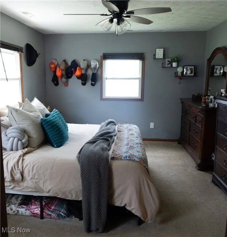 Bedroom with light colored carpet, multiple windows, and ceiling fan