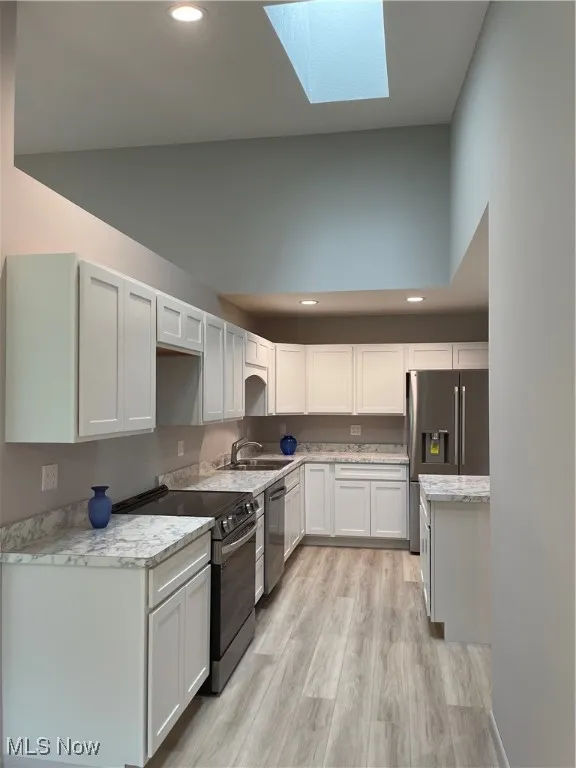 Kitchen featuring recessed lighting, range, a skylight, light wood-type flooring, and white cabinets