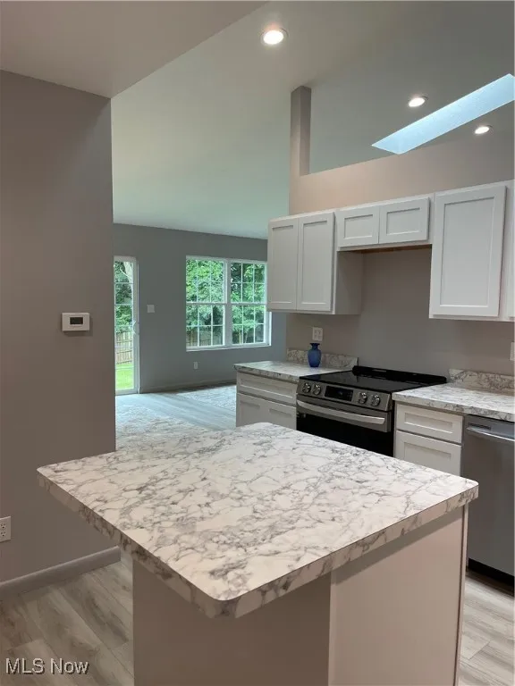Kitchen with a skylight, stove, light countertops, recessed lighting, and light wood-style flooring