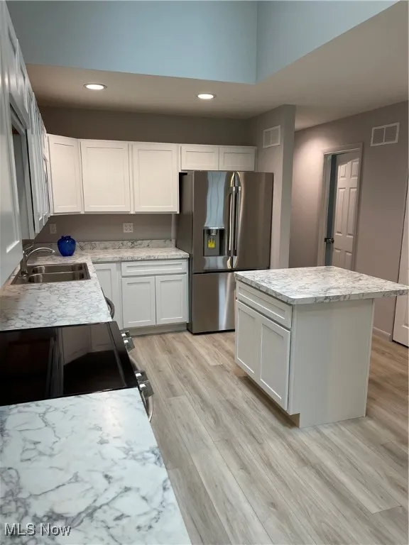 Kitchen with freestanding refrigerator, range, a kitchen island, light wood finished floors, and recessed lighting