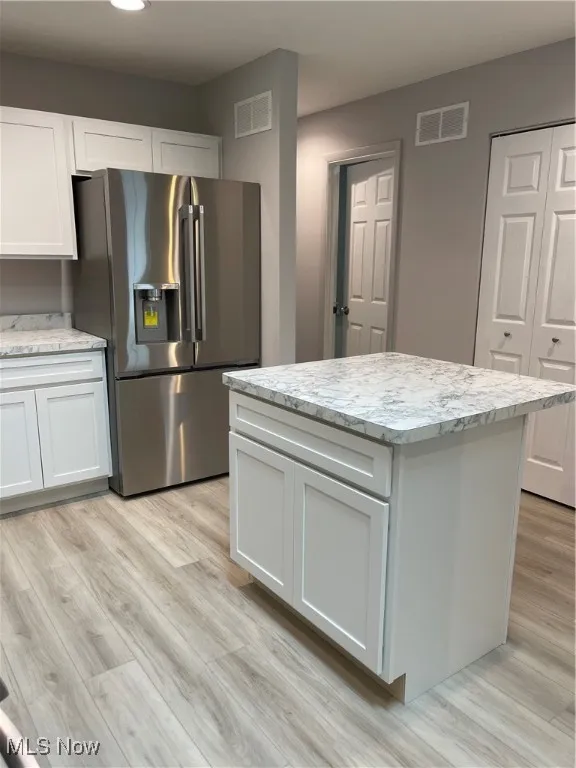 Kitchen with fridge, white cabinets, light wood-type flooring, and a center island