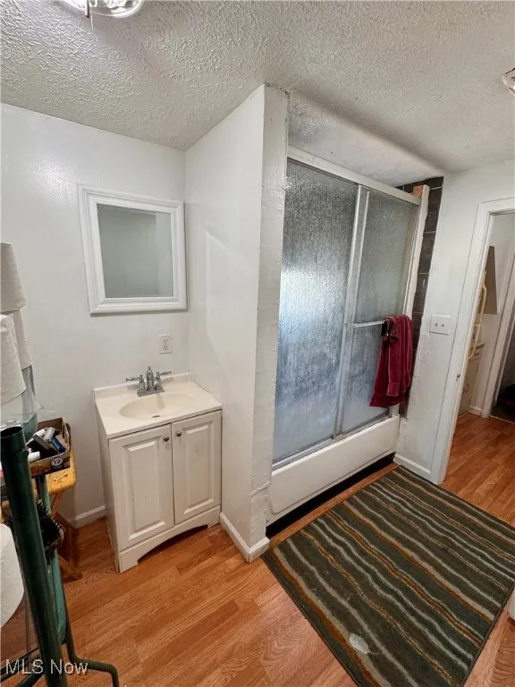 Full bath with a textured ceiling, vanity, wood finished floors, and combined bath / shower with glass door