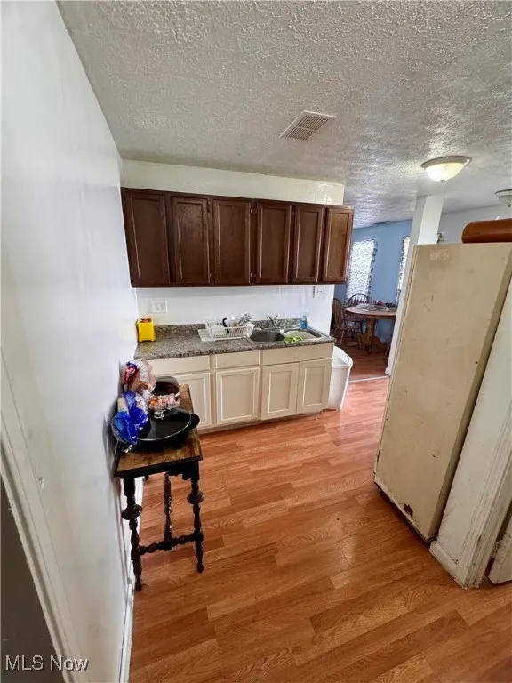 Kitchen with freestanding refrigerator, light wood-type flooring, a textured ceiling, and dark brown cabinetry