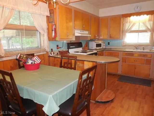 Kitchen with stove, light wood-type flooring, white microwave, under cabinet range hood, and brown cabinetry