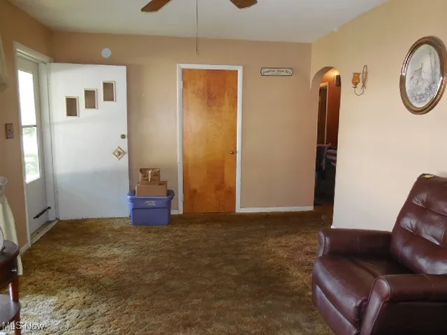 Living area with arched walkways, ceiling fan, and carpet floors