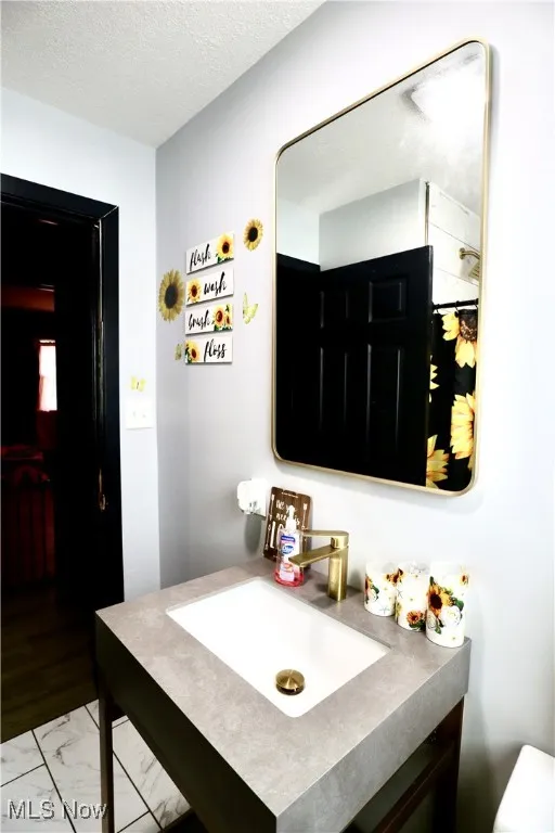 Bathroom with vanity, a textured ceiling, and marble look tile flooring