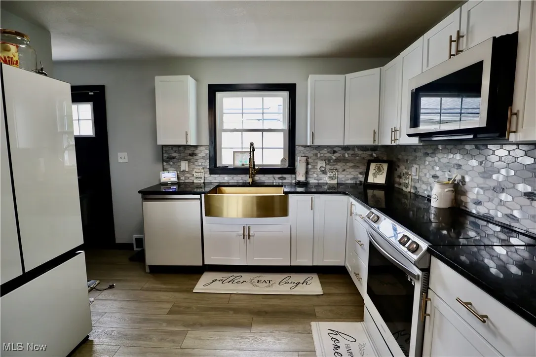 Kitchen featuring appliances with stainless steel finishes, wood finished floors, white cabinets, and dark countertops