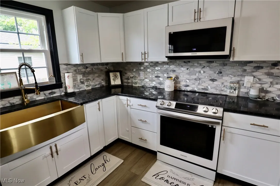 Kitchen with electric stove, white microwave, white cabinets, dark wood finished floors, and backsplash