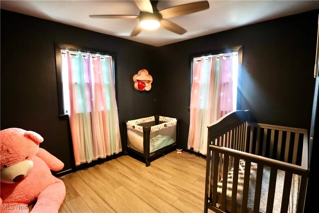Bedroom with wood finished floors, a crib, and a ceiling fan