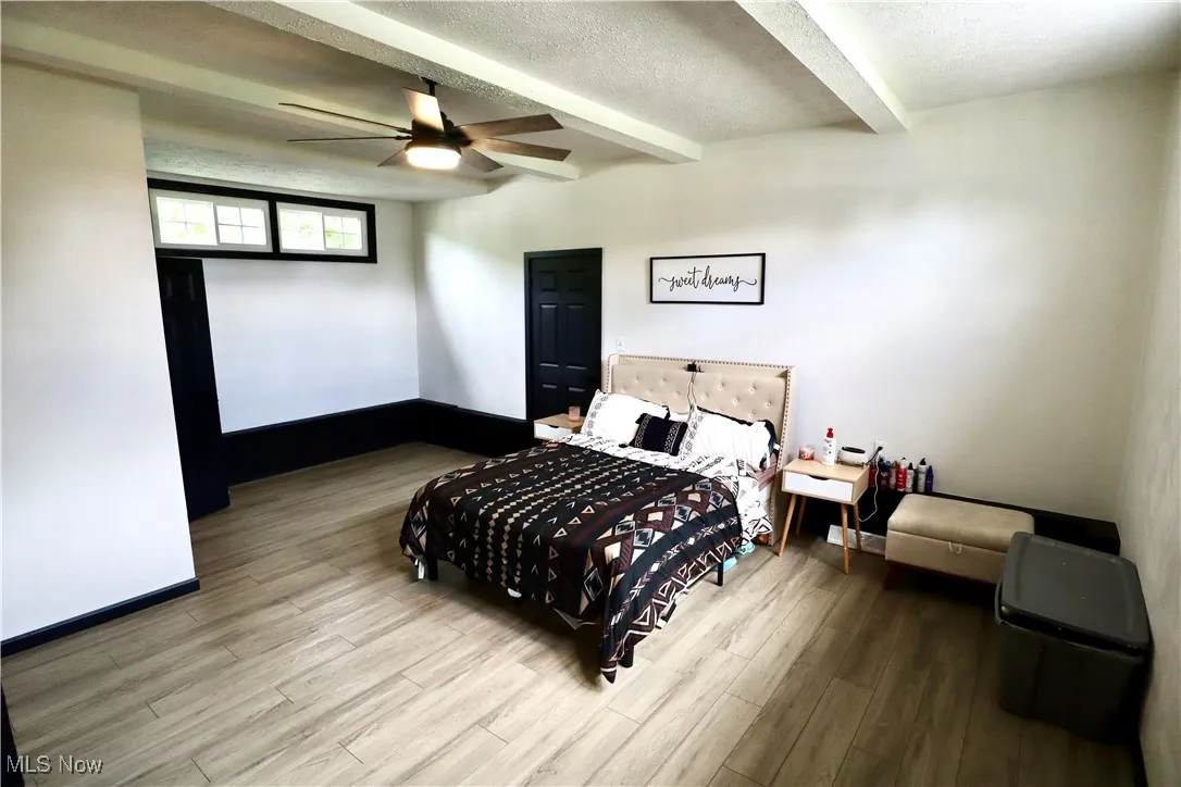 Bedroom featuring beam ceiling, wood finished floors, a textured ceiling, and a ceiling fan