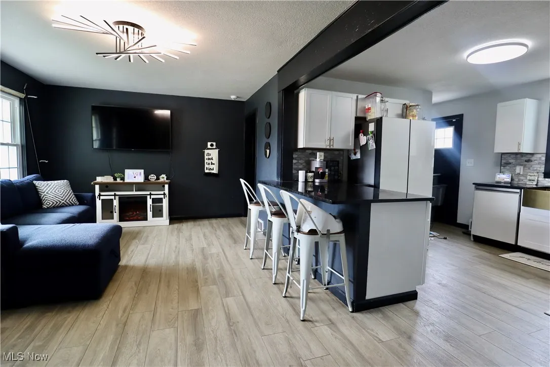 Kitchen featuring dark countertops, a breakfast bar area, stainless steel dishwasher, white cabinets, and a textured ceiling