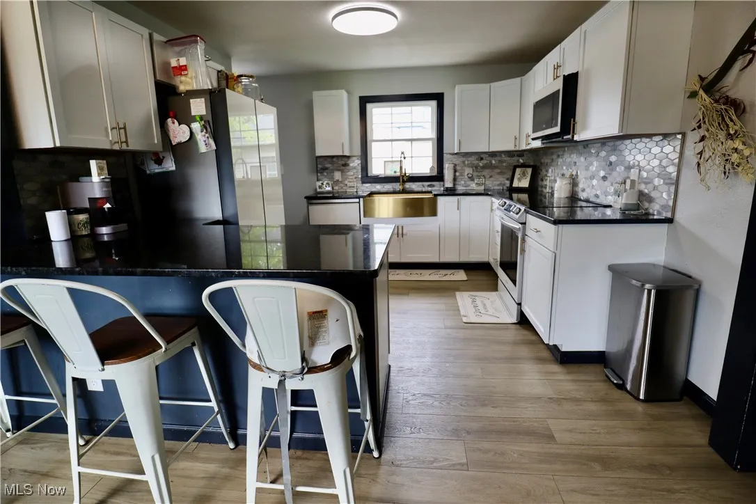 Kitchen featuring electric range, a peninsula, tasteful backsplash, and dark countertops