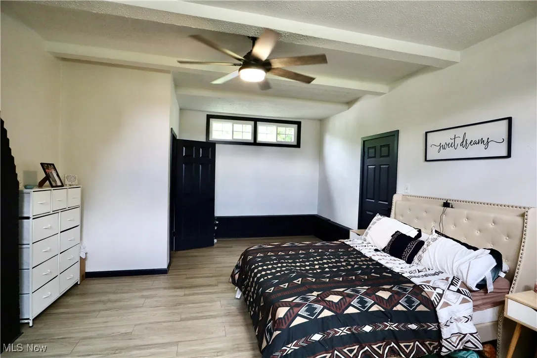 Bedroom with light wood-type flooring, beam ceiling, a textured ceiling, and a ceiling fan