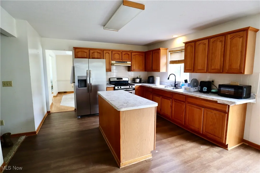Kitchen featuring appliances with stainless steel finishes, light countertops, a center island, backsplash, and dark wood-style flooring