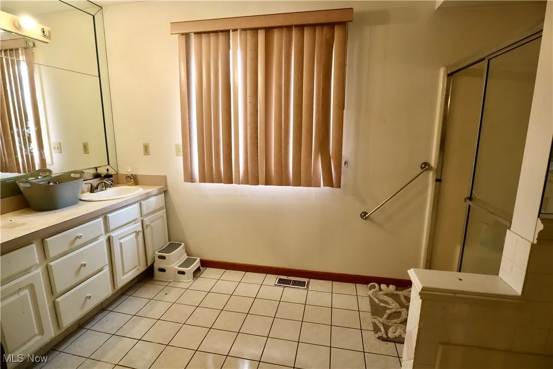 Full bath with double vanity, tile patterned floors, and a stall shower