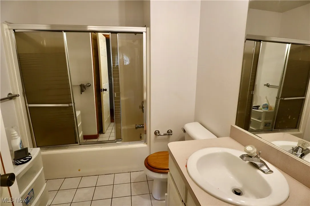 Full bath with tile patterned floors, combined bath / shower with glass door, and vanity