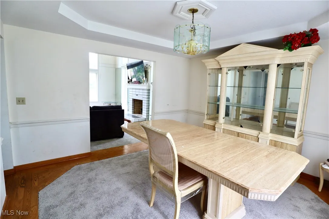 Dining room with a brick fireplace, wood finished floors, a raised ceiling, and a chandelier
