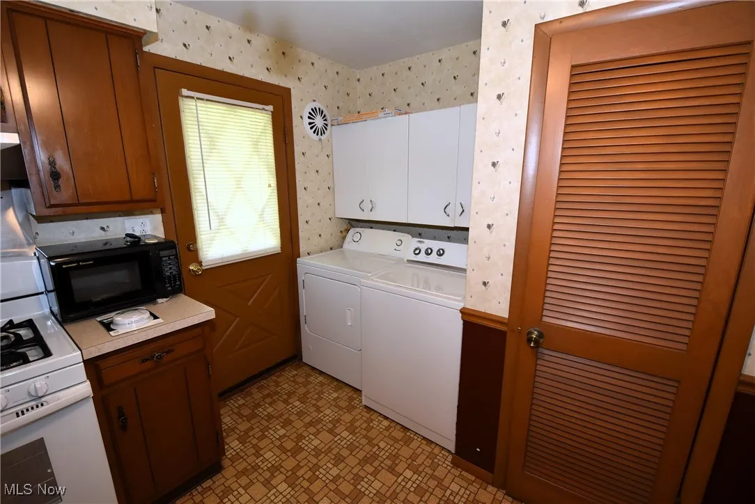 Laundry room with washing machine and clothes dryer, light floors, and wallpapered walls