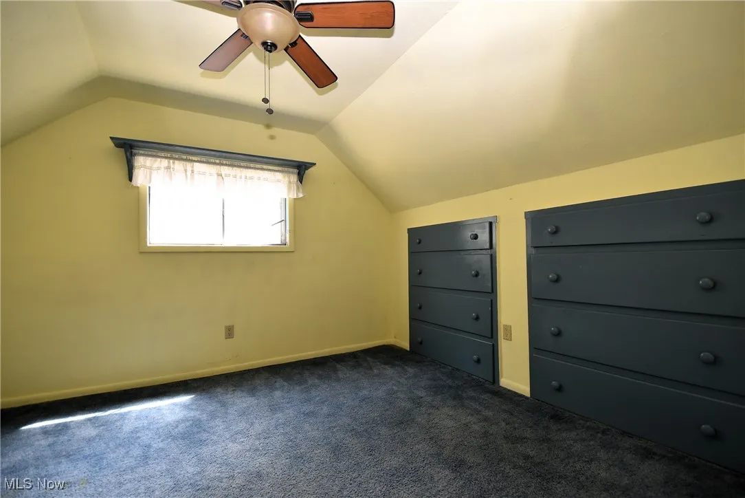 Bonus room with vaulted ceiling, dark carpet, and a ceiling fan