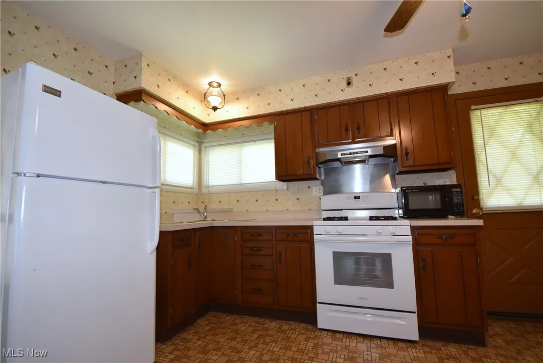 Kitchen featuring white appliances, brown cabinets, wallpapered walls, and tile patterned floors