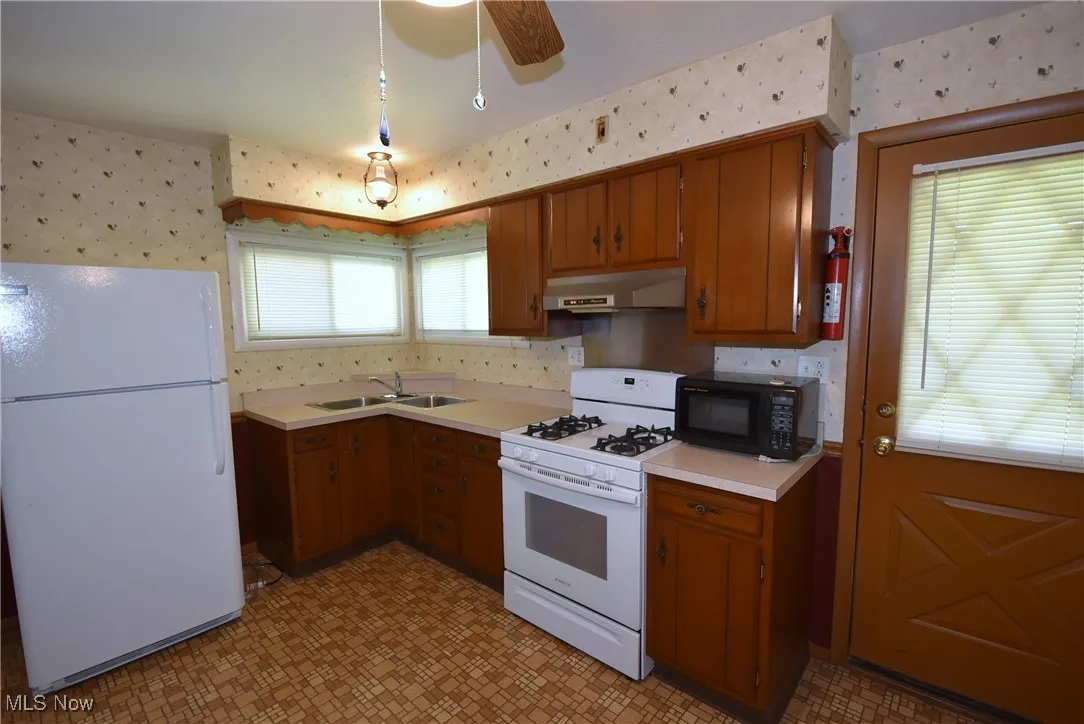 Kitchen featuring wallpapered walls, white appliances, brown cabinets, and light floors