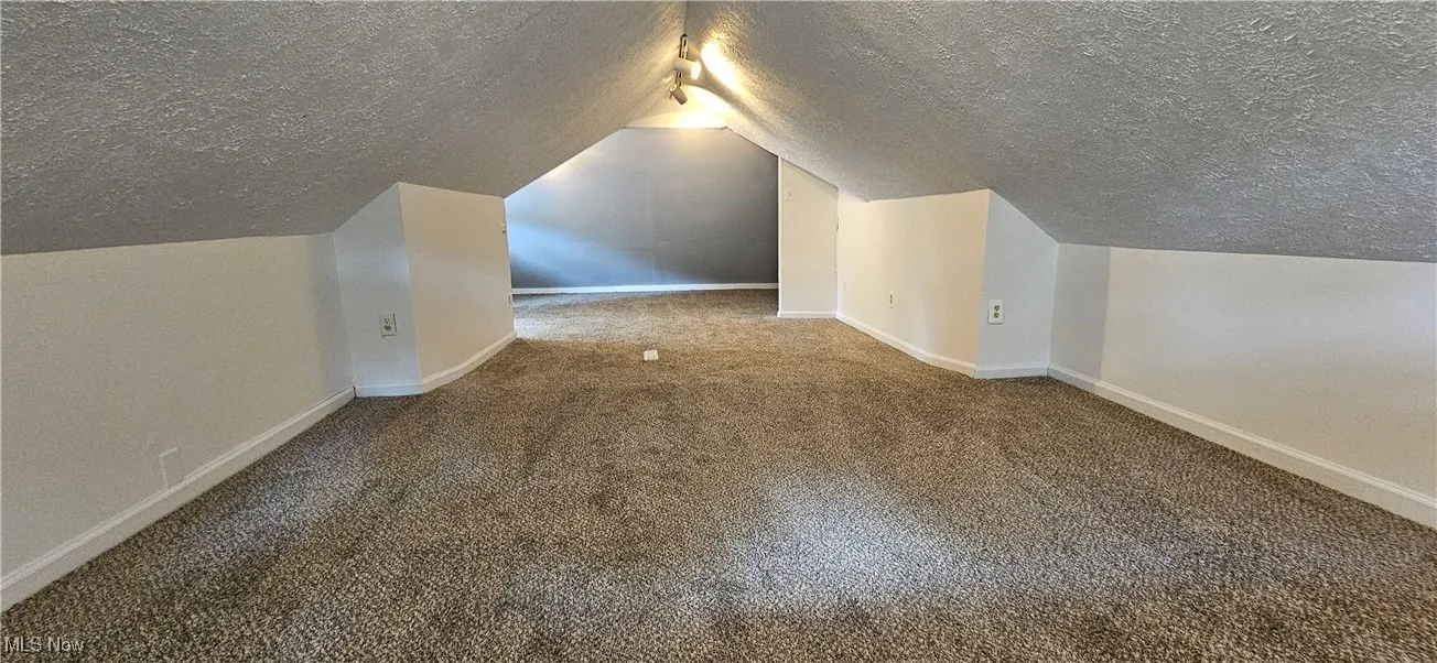 Third bedroom featuring a textured ceiling, new carpet flooring, and vaulted ceiling
