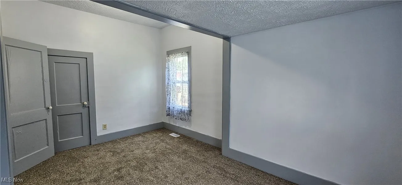 First bedroom featuring a textured ceiling and new carpet