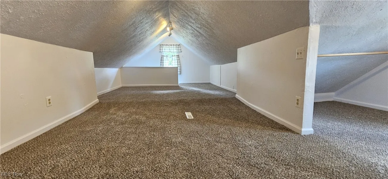 Third bedroom with a textured ceiling, new carpet, and vaulted ceiling