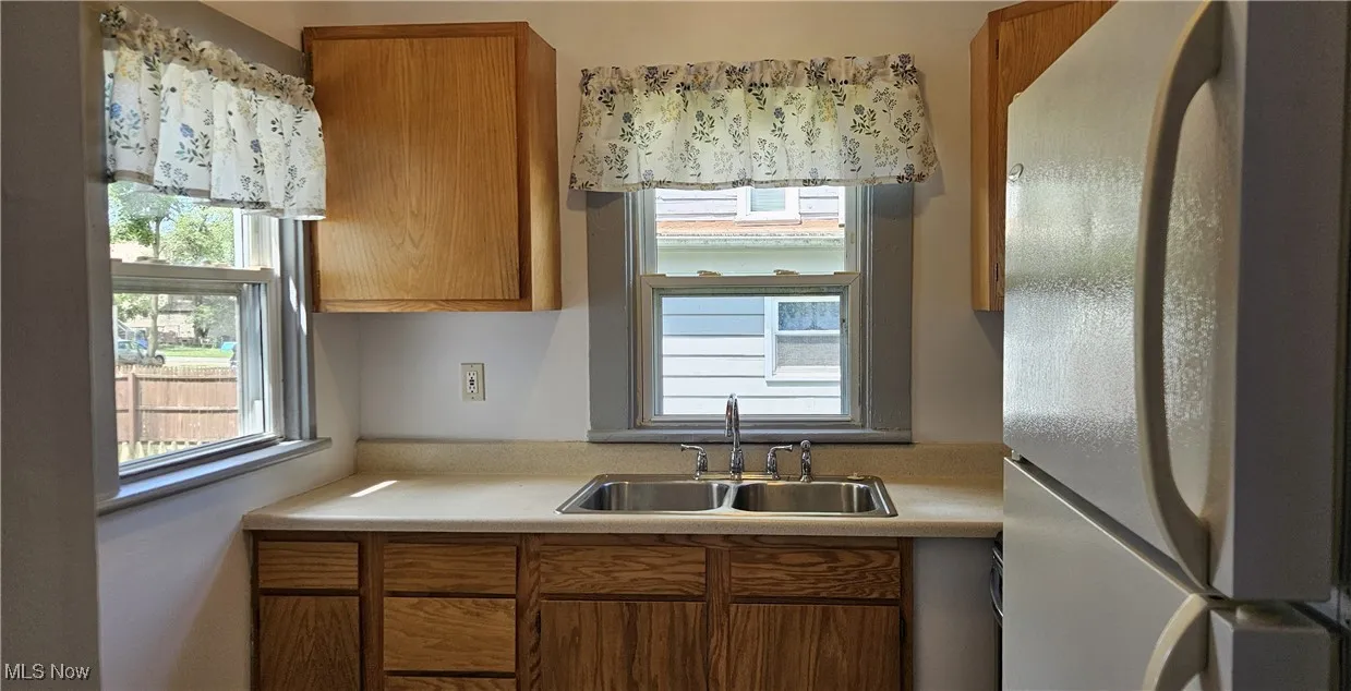 Kitchen with freestanding refrigerator, light countertops, brown cabinetry, and plenty of natural light