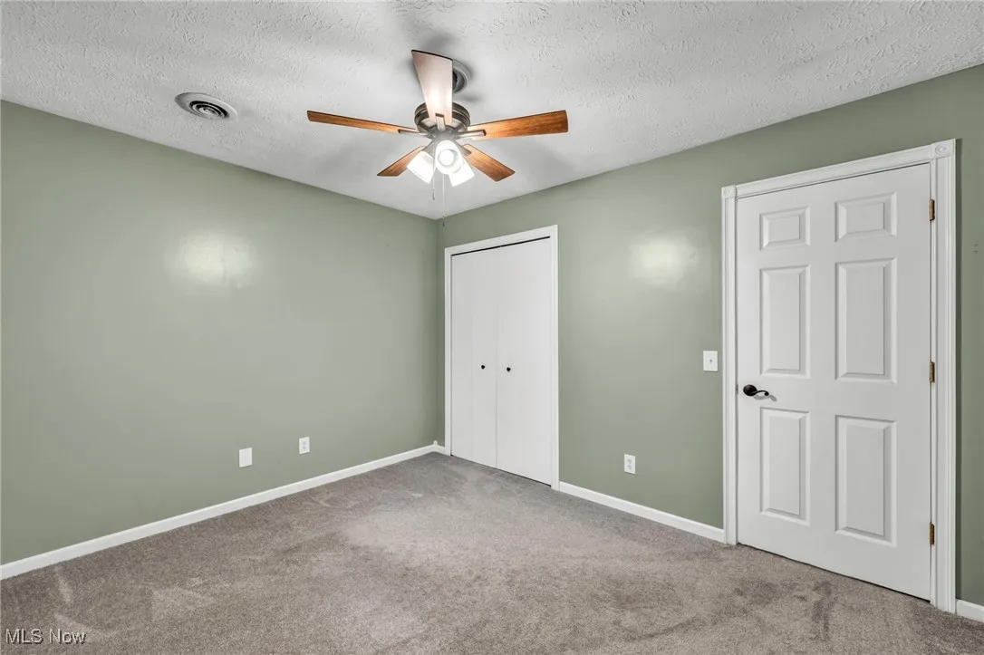 Unfurnished bedroom featuring a textured ceiling, carpet, a closet, and ceiling fan