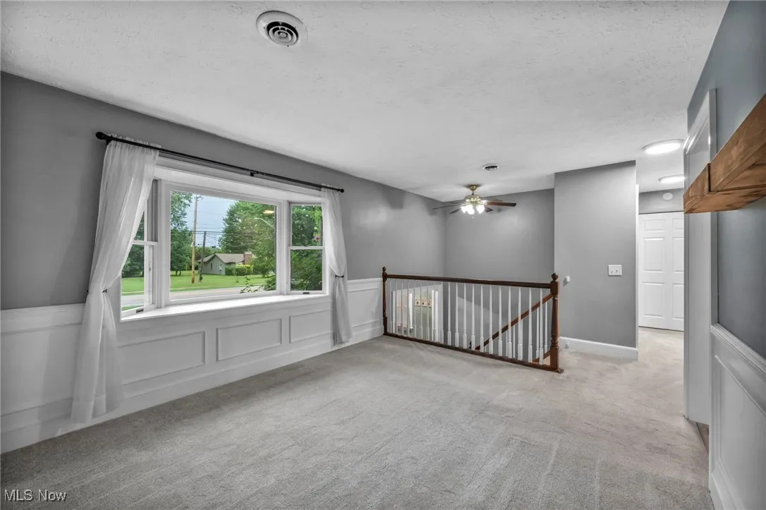 Empty room with a decorative wall, wainscoting, carpet floors, a textured ceiling, and a ceiling fan