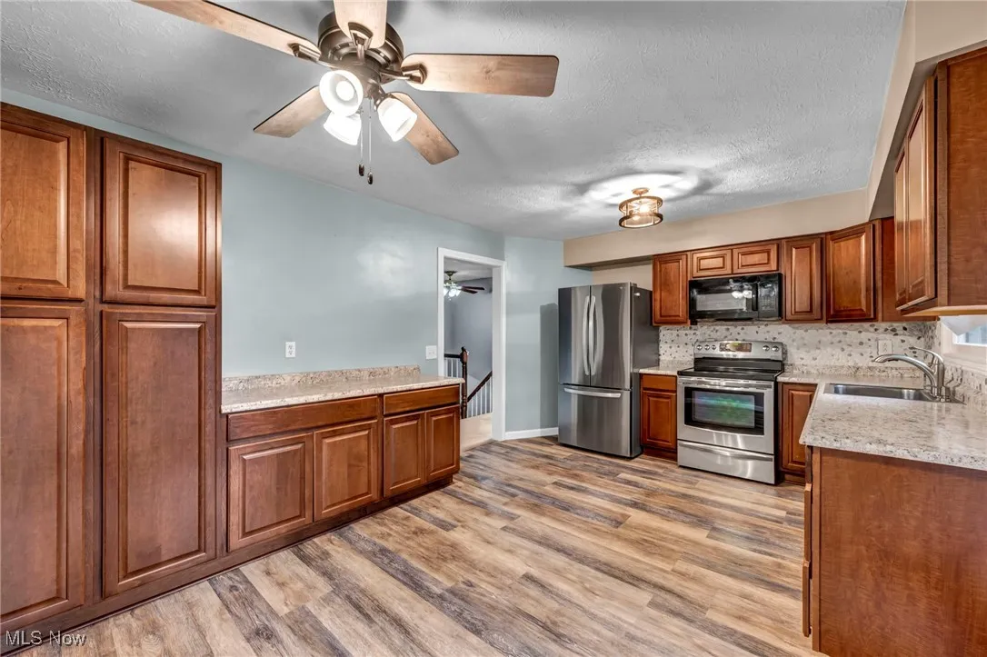Kitchen featuring stainless steel appliances, ceiling fan, a textured ceiling, brown cabinetry, and decorative backsplash