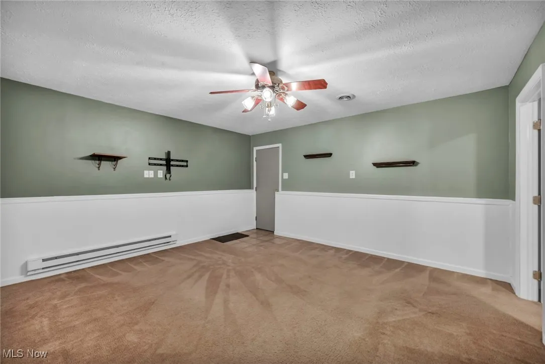 Empty room featuring baseboard heating, ceiling fan, a textured ceiling, and carpet