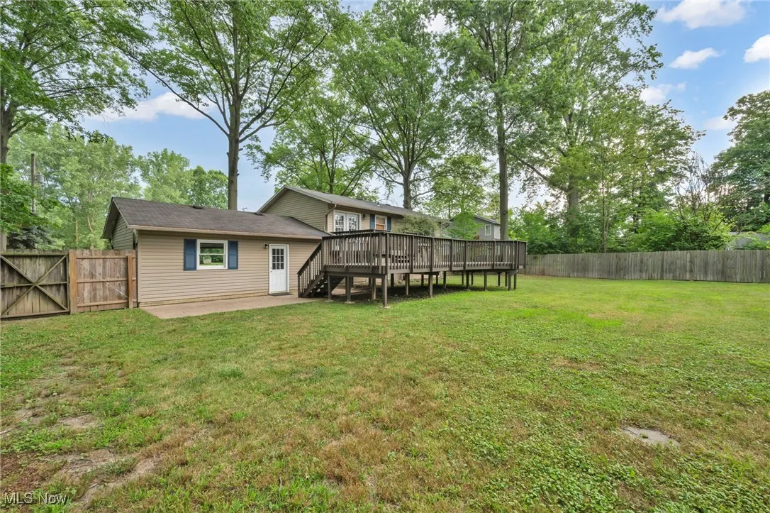 Rear view of property featuring a wooden deck, a fenced backyard, a gate, and view of scattered trees