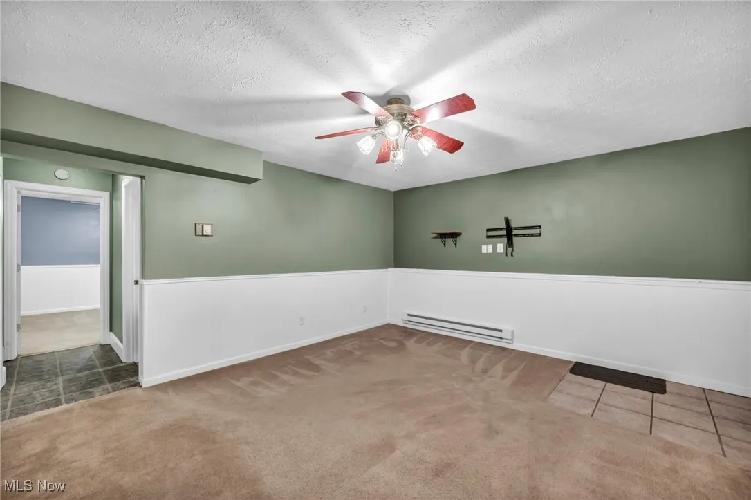 Carpeted empty room with wainscoting, ceiling fan, baseboard heating, a textured ceiling, and tile patterned flooring