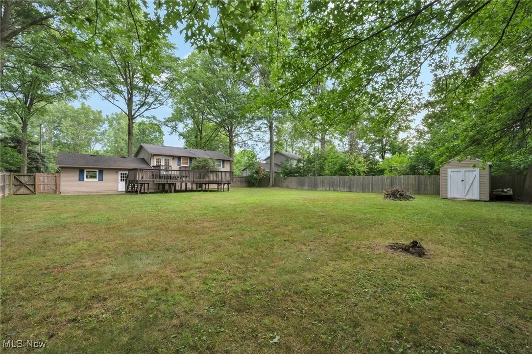 Fenced backyard featuring a shed, a wooden deck, and view of scattered trees