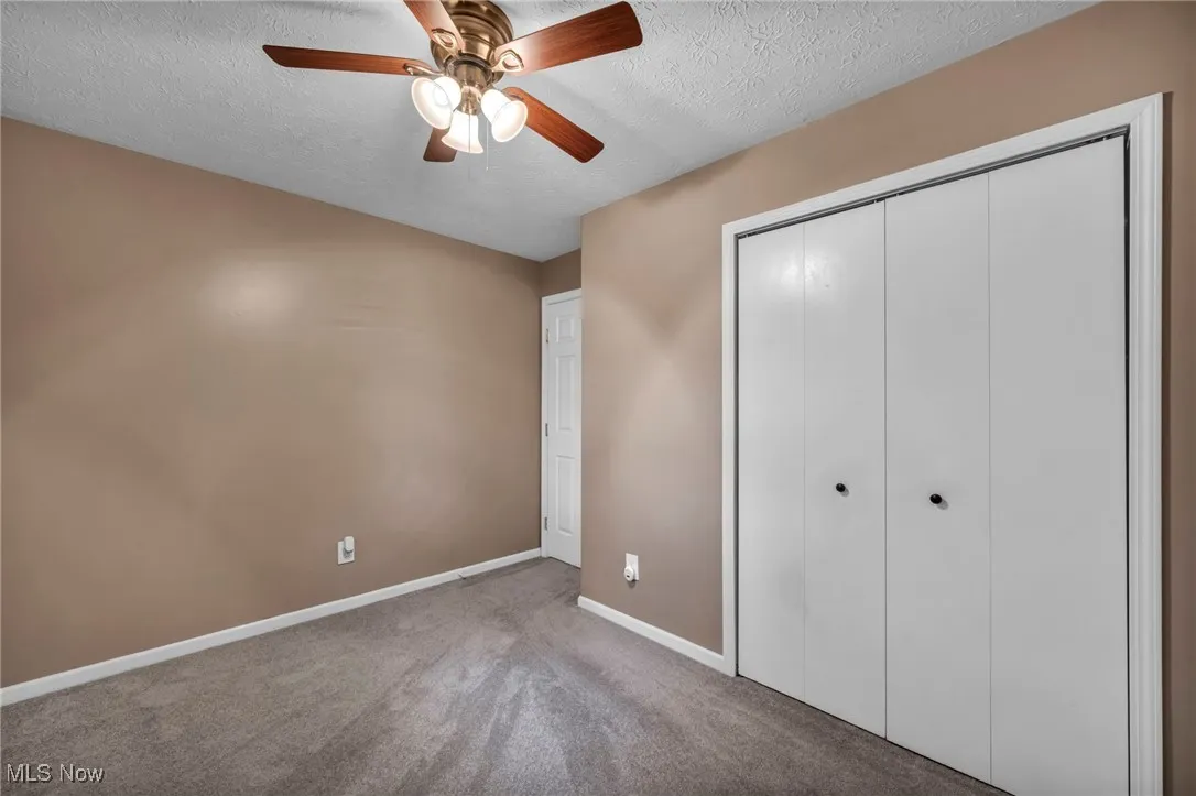 Unfurnished bedroom with a textured ceiling, carpet flooring, a closet, and ceiling fan