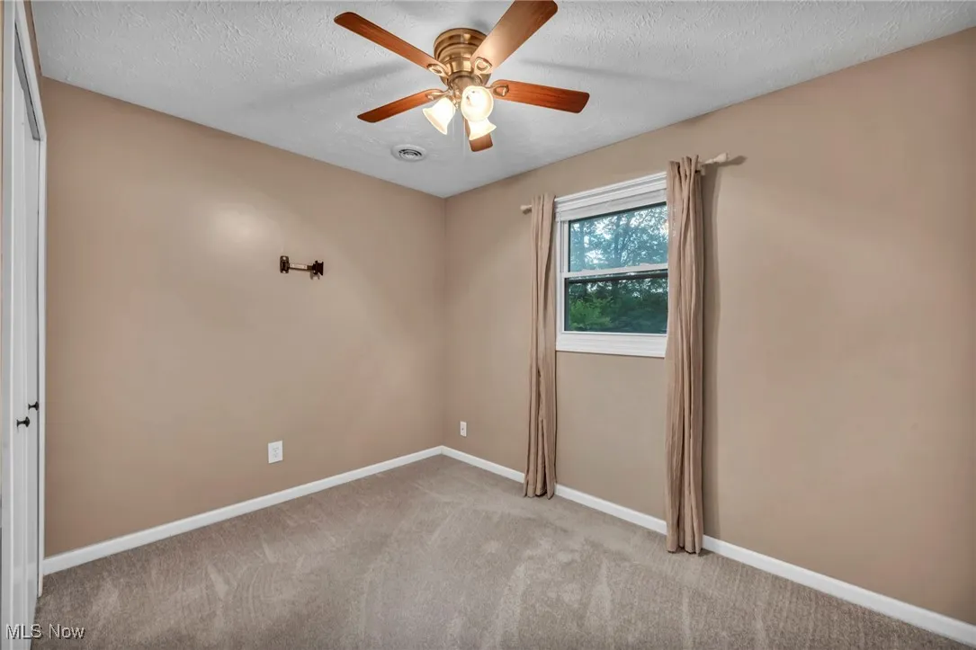 Carpeted empty room featuring a textured ceiling and ceiling fan