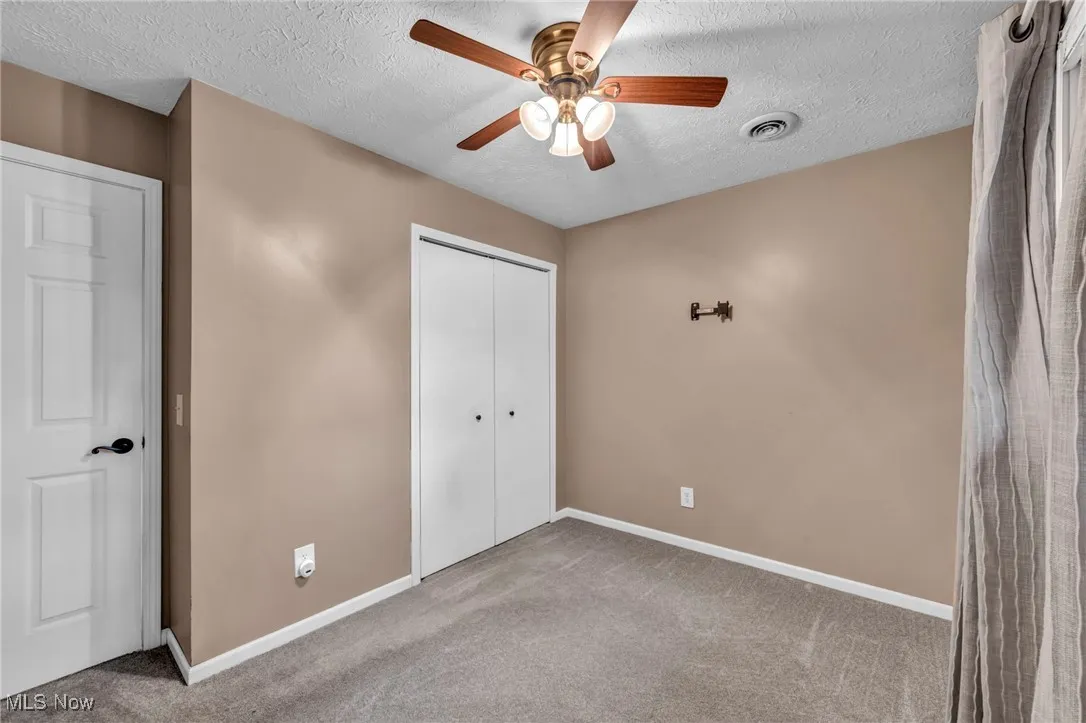 Unfurnished bedroom featuring carpet, a textured ceiling, a closet, and a ceiling fan