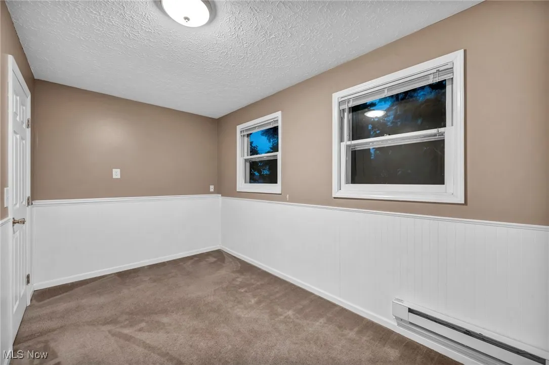 Carpeted empty room with baseboard heating, a textured ceiling, and wainscoting